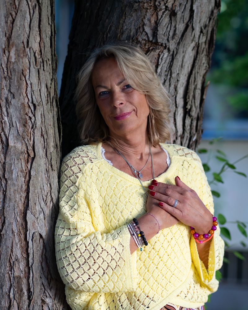 Anke Elsa Delfs an einen Baum gelehnt, eine Hand auf dem Herzen.