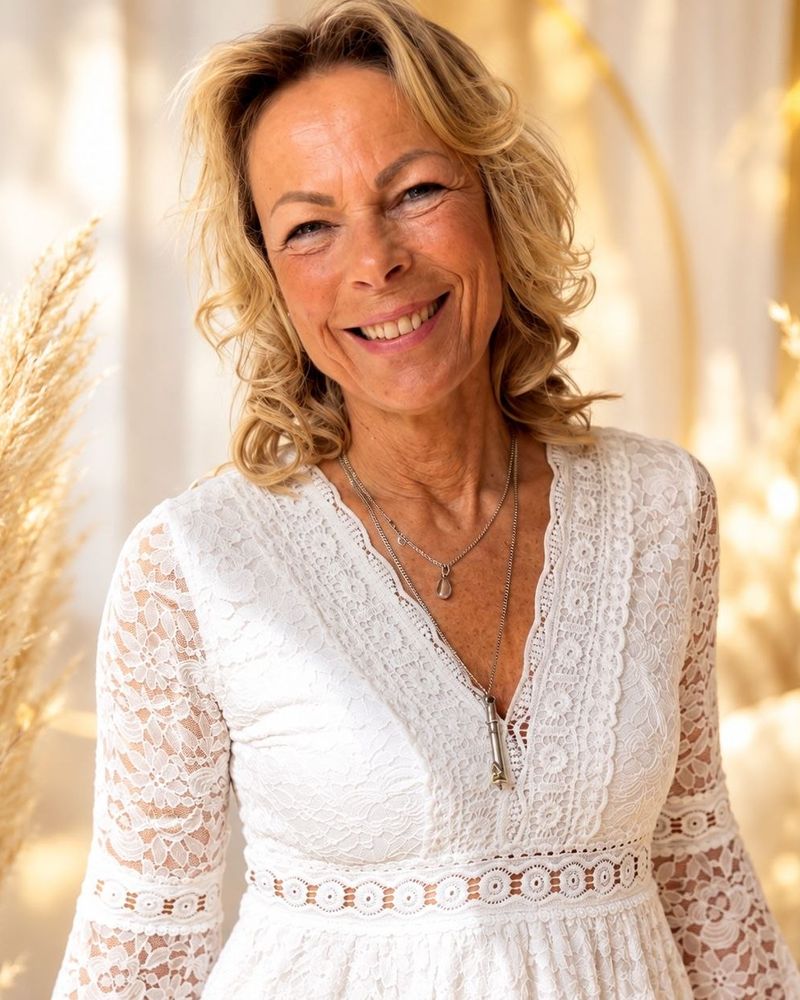 Anke Elsa Delfs in einem weißen Spitzenkleid vor goldenem Licht.